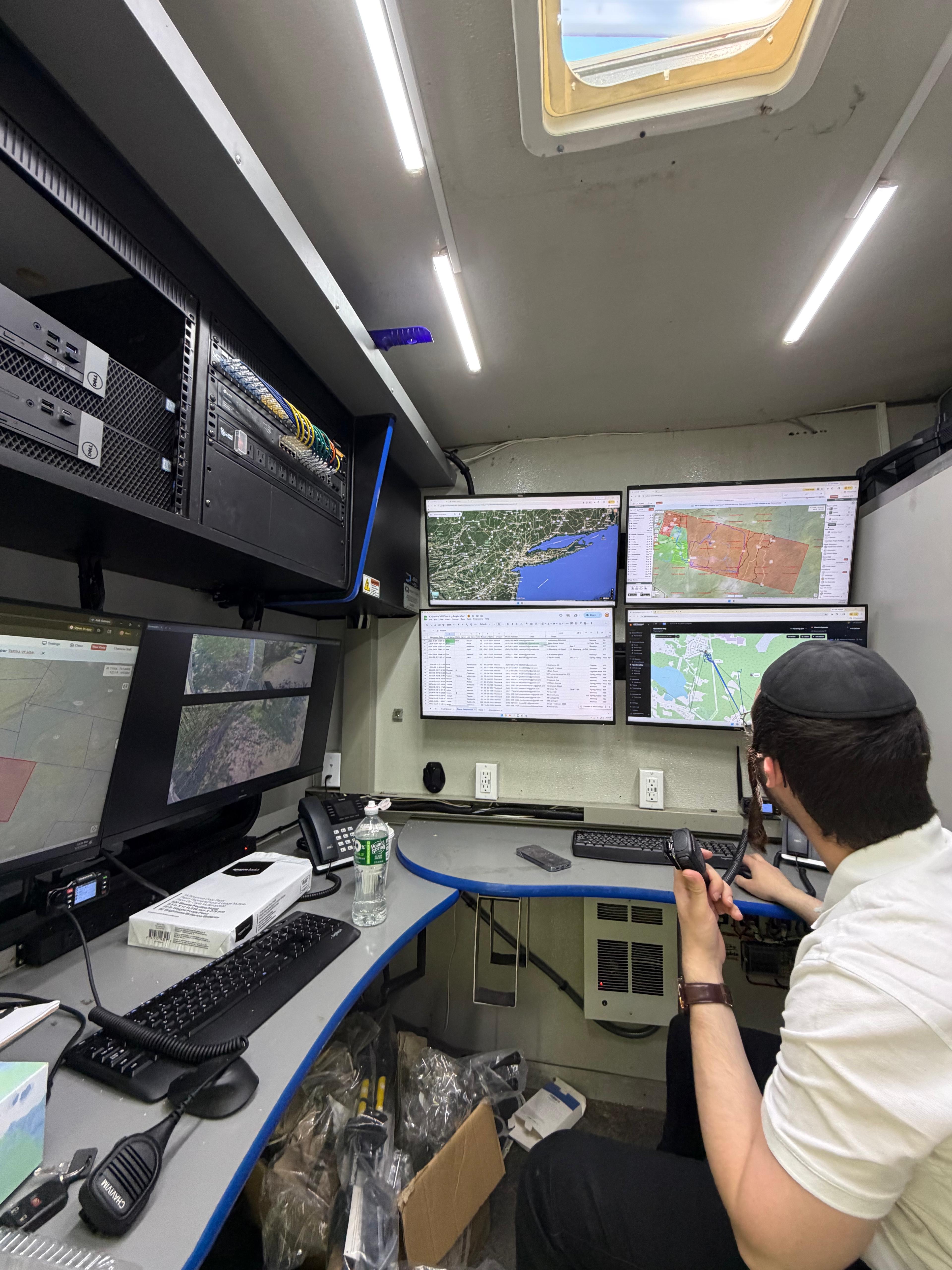 Wide interior view of the KJ-500 SAR Command Center with equipment racks, monitors, mapping software, and an active command operator