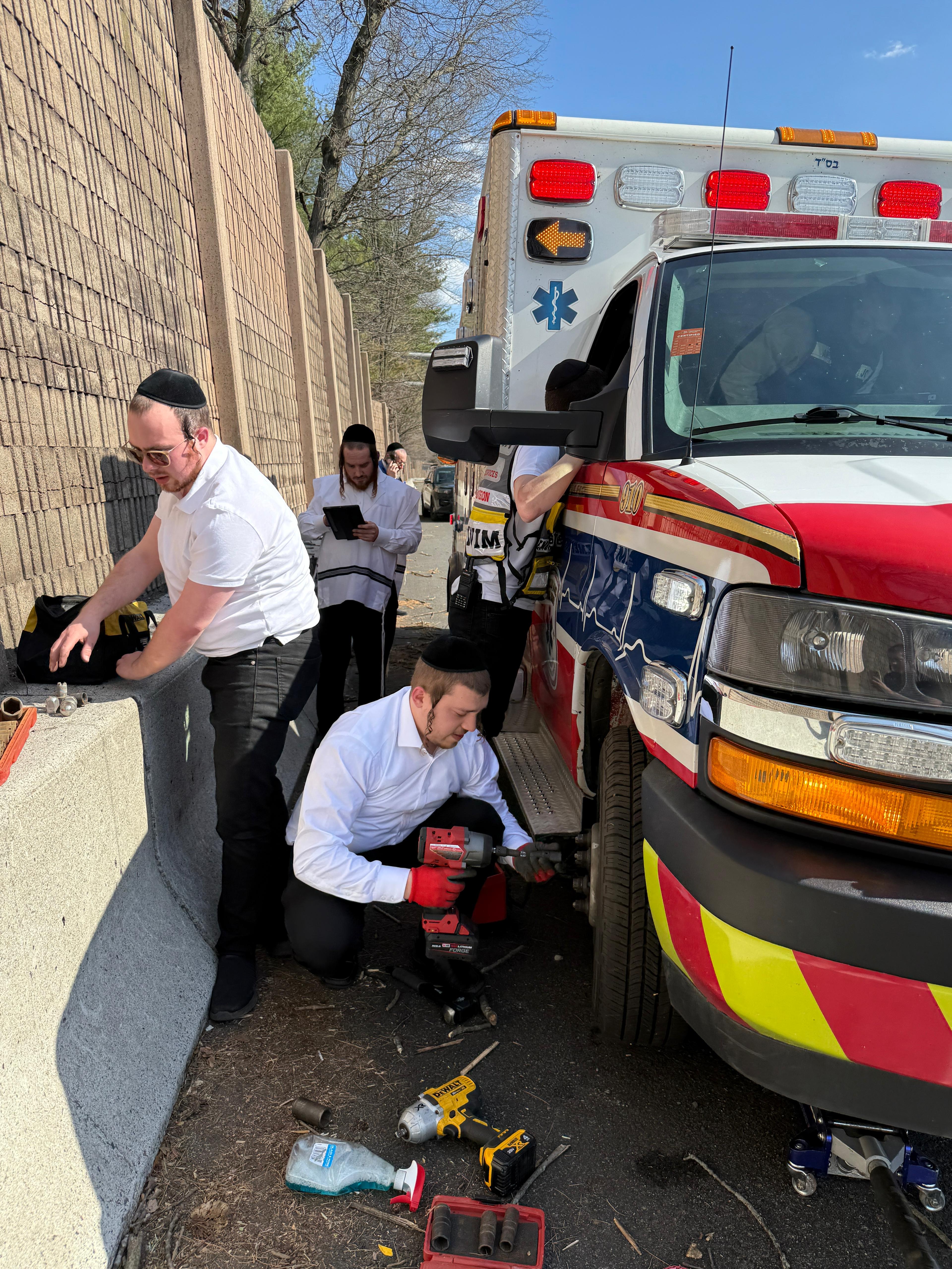 Chavivim members using power tools to mount the spare tire on the KJ Hatzalah ambulance on the shoulder of Route 17